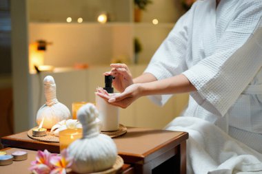 Bornozlu kadın avucuna şişeden aromatik yağ pompalıyor. Lüks bir kaplıcada cilt bakımı ve sağlık konsepti. Profesyonel terapi..