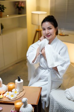 Kadın, pofuduk beyaz bir havluyla yüzünü mum, çiçek, bitkisel kompres, sağlıklı yaşam ve gençleşme ile kaplıcaya siliyor..