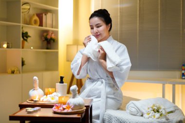 Kadın, pofuduk beyaz bir havluyla yüzünü mum, çiçek, bitkisel kompres, sağlıklı yaşam ve gençleşme ile kaplıcaya siliyor..