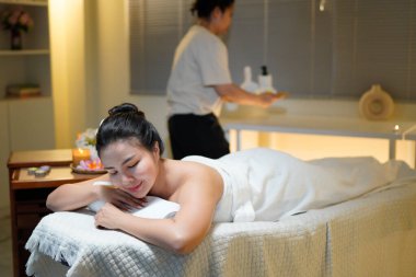 Masaj stüdyosuna gelen bir ziyaretçi güzellik salonunun sakin atmosferinde rahatlar. Masözle masaj yapan genç bir kadın, arka plandaki ekipmanı hazırlar..