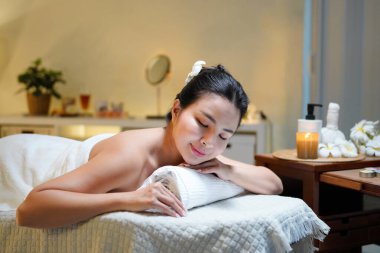 Bir sağlık merkezinde masaj masasında uzanmış, siyah saçlı, güzel bir kadın..