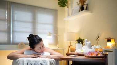 Bir sağlık merkezinde masaj masasında uzanmış, siyah saçlı, güzel bir kadın..