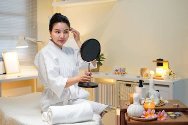 Mutlu spa müşterileri. Kozmetik bilimi sonucu. Profesyonel hizmet. Güzellik salonundaki kozmetik uzmanı yüz prosedüründen sonra aynada pürüzsüz, temiz bir cildin keyfini çıkaran memnun kadın müşteri..