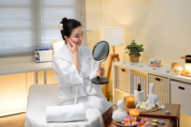 Mutlu spa müşterileri. Kozmetik bilimi sonucu. Profesyonel hizmet. Güzellik salonundaki kozmetik uzmanı yüz prosedüründen sonra aynada pürüzsüz, temiz bir cildin keyfini çıkaran memnun kadın müşteri..