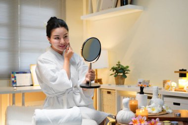 Mutlu spa müşterileri. Kozmetik bilimi sonucu. Profesyonel hizmet. Güzellik salonundaki kozmetik uzmanı yüz prosedüründen sonra aynada pürüzsüz, temiz bir cildin keyfini çıkaran memnun kadın müşteri..