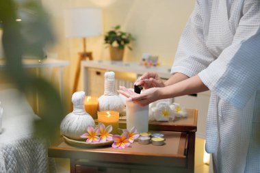 Bornozlu kadın avucuna şişeden aromatik yağ pompalıyor. Lüks bir kaplıcada cilt bakımı ve sağlık konsepti. Profesyonel terapi..