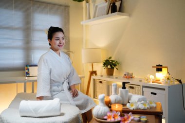 Bornozlu kadın güzellik salonunda huzur ve lüks içinde oturuyor. Spa 'da masaj masasında oturup meditasyon yapan sakin bir kadının profili. Boşluğu kopyala.