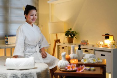 Bornozlu kadın güzellik salonunda huzur ve lüks içinde oturuyor. Spa 'da masaj masasında oturup meditasyon yapan sakin bir kadının profili. Boşluğu kopyala.