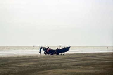 Bir grup insan, deniz kıyısında sakin bir sahilde tekneyi itiyor.
