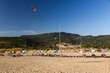 Şemsiyeli Renkli Sahil Sahnesi ve Canlı Uçurtmalar Bir Dağ Arkaplanına Karşı