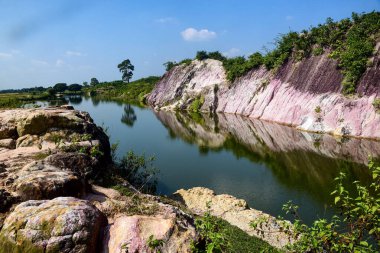 Pink Striped Cliff Landscape Reflected In Calm Water Under Blue Sky