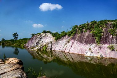 Pink Striped Cliff Landscape Reflected In Calm Water Under Blue Sky