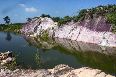 Pink Striped Cliff Landscape Reflected In Calm Water Under Blue Sky