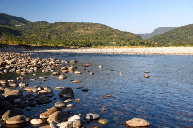 Scenic Riverbank With Pebbles and Tubes Under Clear Blue Sky