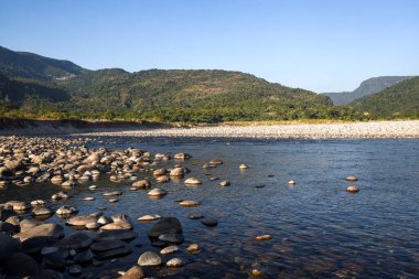 Scenic Riverbank With Pebbles and Tubes Under Clear Blue Sky