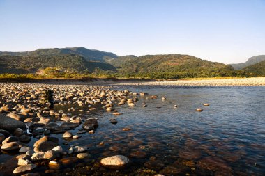Scenic Riverbank With Pebbles and Tubes Under Clear Blue Sky