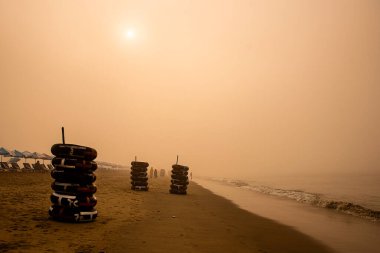 Sunrise 'da Yığılmış İç Tüpler ve Şemsiyelerle Misty Beach Sahnesi