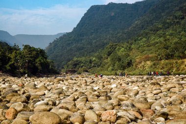İnsanlar yemyeşil tepeler ve dağ vadileri arasında Kayalık Nehir yatağını keşfediyor.