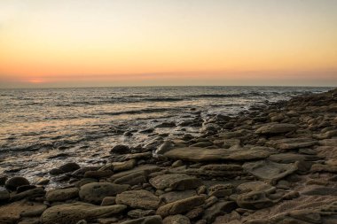 Coastal Rocky Shoreline at Sunrise with Serene Orange Sky and Calm Waves