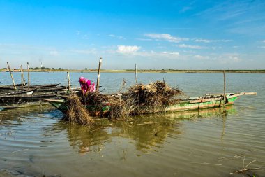 Parlak pembe elbiseli bir kadın sakin bir gölün kıyısındaki kırsal bir balıkçı teknesinde ağ örmeye eğilimlidir. Basit, suyun üzerindeki günlük yaşam, zanaat ve emeğe odaklı..