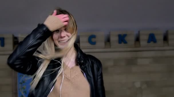 Vonzó lány hosszú szőke haj, a bőr kabát kiegyenesedik haj állt a háttérben egy vonat jön a metró — Stock videók