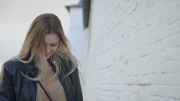 Linda chica con pelo largo y rubio en chaqueta de cuero posando en la ciudad endereza el cabello slo-mo — Vídeos de Stock