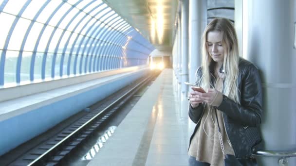 Mladá dívka s dlouhými blonďatými vlasy miniaplikaci v kožené bundě s narovnává vlasy v metru na pozadí vlak přijíždí, Rusko, Kazan, 22.04.2016 — Stock video