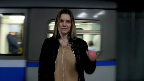 Aantrekkelijk meisje met lang blond haar in lederen jas met rechtmaakt haren draagkracht in metro tegen de achtergrond van een trein komt, Rusland, Kazan, 22.04.2016 — Stockvideo