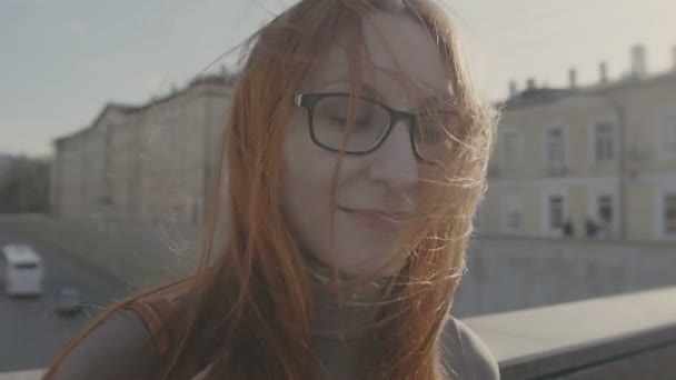 Mooi meisje met rood haar dragen van een bril in straat dichtbij snelweg kijkt in de camera slo-mo — Stockvideo