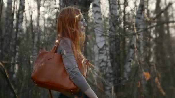 Bella ragazza con i capelli rossi indossando occhiali va nel parco — Video Stock