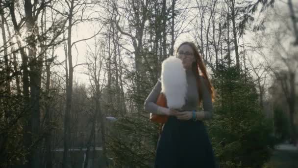 Beautiful girl with red hair wearing glasses eating cotton candy at dusk — Stock Video
