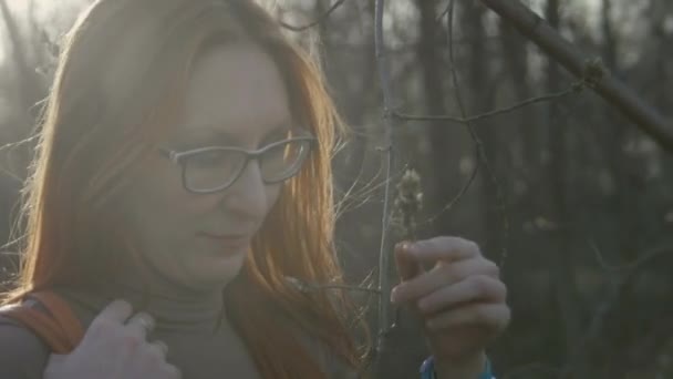 Menina bonita com cabelo vermelho usando óculos no parque tenta morder salgueiro — Vídeo de Stock