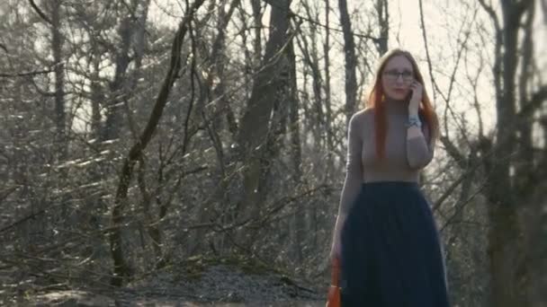 Hermosa chica con el pelo rojo con gafas en el parque hablando por teléfono de cerca — Vídeos de Stock