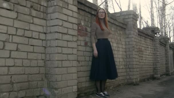 Красива дівчина з рудим волоссям в окулярах, що стоять біля цегляної стіни і колючого дроту — стокове відео