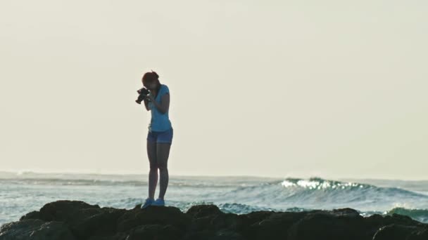 Linda joven con el pelo rojo en gafas va en las rocas y fotografías vida marina en el mar Caribe frente a las olas en República Dominicana, teleobjetivo, cámara lenta — Vídeos de Stock