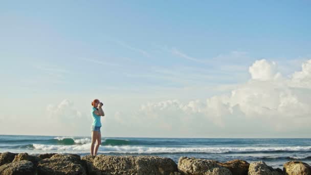 Młoda kobieta z rude włosy w okulary fotografie morza stojąc na skały, beach Dominikana, szeroki kąt — Wideo stockowe