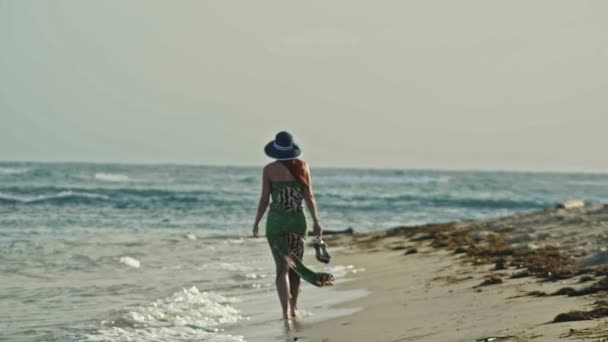 Mujer joven En vestido largo mantiene los zapatos y caminar a lo largo del mar, alejarse, cámara lenta, gran ángulo — Vídeos de Stock