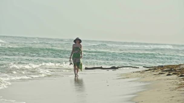 Jonge vrouw In lange jurk houdt schoenen en wandelen langs de zee, slow-motion — Stockvideo