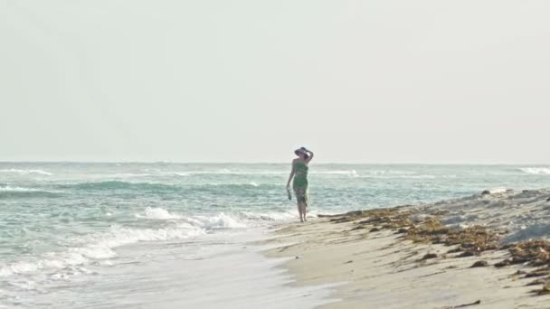 Junge Frau im langen Kleid behält die Schuhe und geht am Meer entlang — Stockvideo