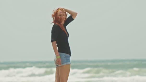 Séduisante fille aux longs cheveux roux debout sur la plage près de la mer de tempête — Video