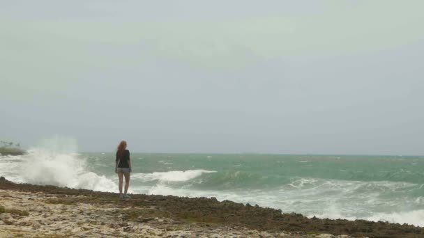 Atrakcyjna, młoda kobieta z długimi rudymi włosami stojący na plaży, w pobliżu morza burza, zwolnionym tempie, szeroki kąt — Wideo stockowe