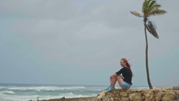 Svůdná dívka s dlouhé červené vlasy sedí na pláži u moře bouří, zpomalené — Stock video