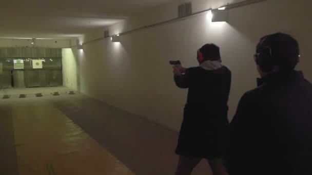 Инструктор наблюдает, как человек стреляет из пистолета в тире — стоковое видео