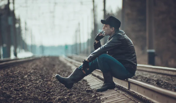 Мужественный человек сидит на железной дороге в лесу и курит — стоковое фото