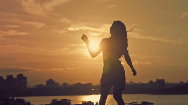 Young attractive girl with flowing hair dancing pirouettes at sunset silhouette — Stockvideo