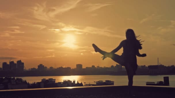 Giovane ragazza attraente con i capelli fluenti sopra il sole che balla il movimento del balletto alla silhouette del tramonto — Video Stock