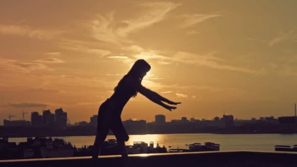 Jeune fille attrayante avec des cheveux fluides dansant mouvements acrobatiques à la silhouette du coucher du soleil — Video