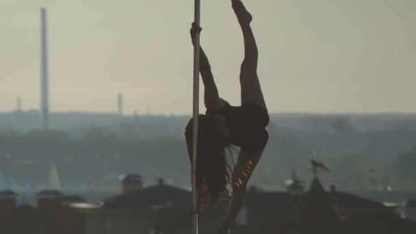 Fit attractive girl in black dress dancing on the portable pole at summer day over the skyline, slow-motion, telephoto — Stock Video