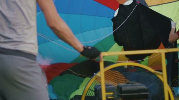 Ein Mann bläst den Umschlag ihres Heißluftballons auf einer Wiese auf — Stockvideo