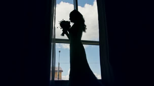 Bride near the window with her wedding bouquet, silhouette — Stock Video